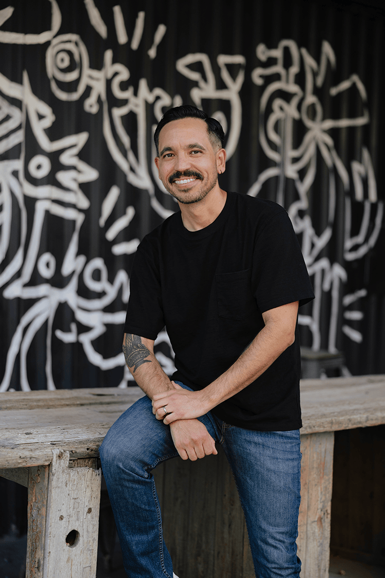 Portrait of Isaac Durazo leaning on a wooden table